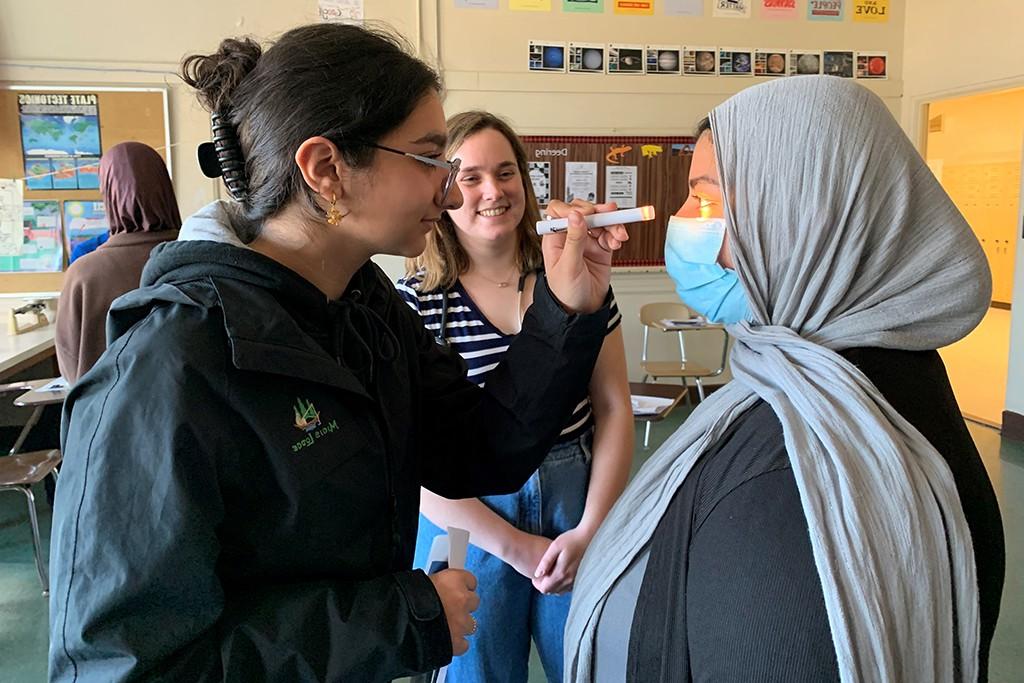  High school student Malak Alobaidi examines UNE student Fajar Alam's eyes during a health assessment exercise