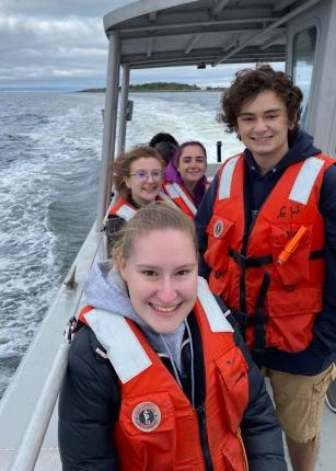 Students smile while wearing lifejackets on a U N E boat