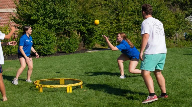 Three students playing a game with a ball and net on the Biddeford campus