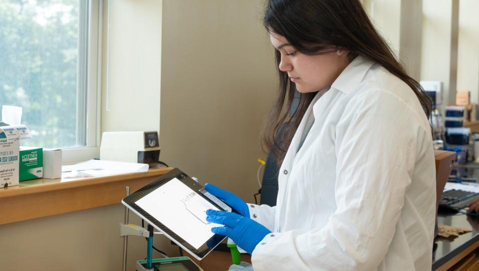 A student in a lab coat touches the graph on a tablet's screen