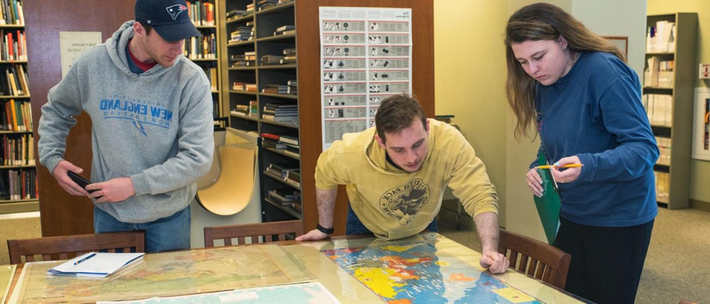 Three U N E Liberal Arts students study a large map in the library