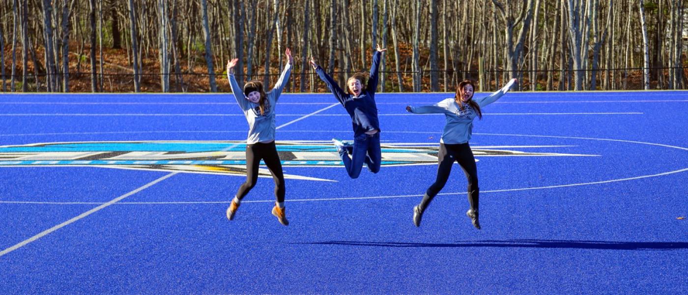 Three students jumping off the Blue Bolt Field on the Biddeford Campus