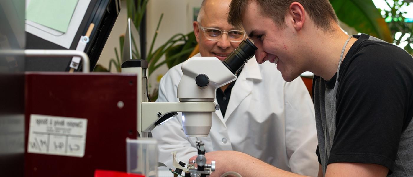 A professor helps as a student peers into a microscope